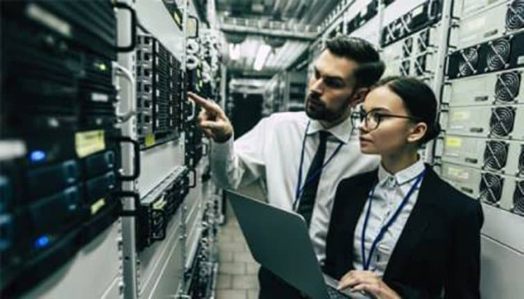 Two engineers with a laptop inspecting equipment in a datacenter aisle